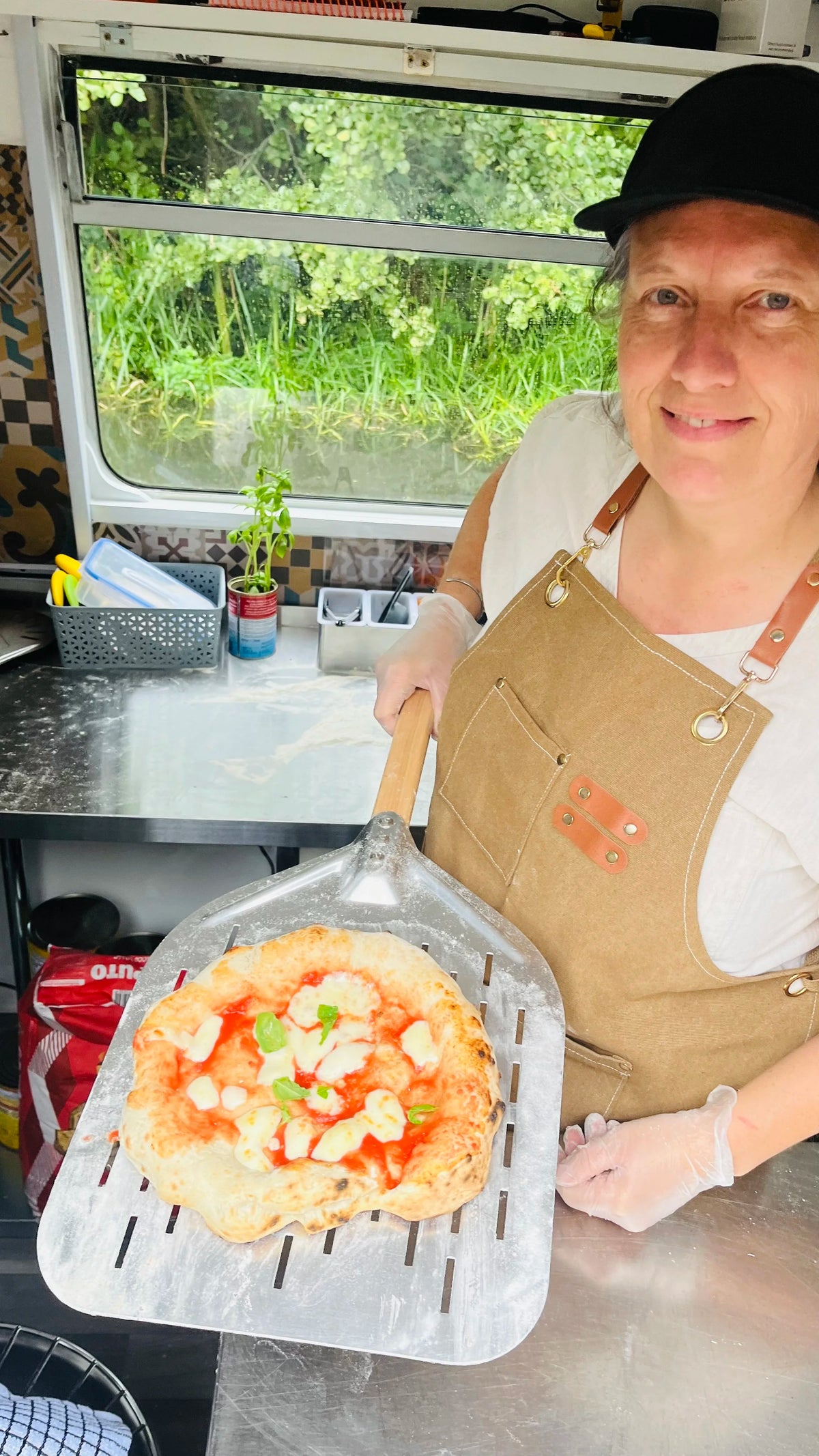 Person holding a pizza on a metal spatula in a kitchen setting
